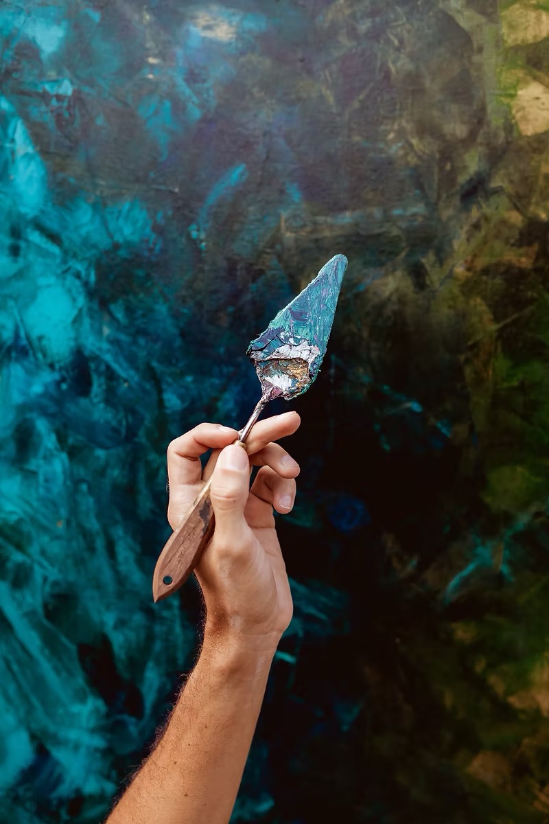Espátula com tinta sobre tela azul-petróleo em processo no ateliê de PH Monteiro